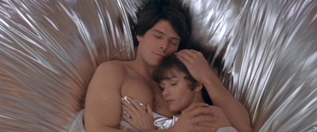 Superman (Christopher Reeve) and Lois Lane (Margot Kidder) enjoy a post-coital cuddle beneath high-tech silver sheets in SUPERMAN II (1981).