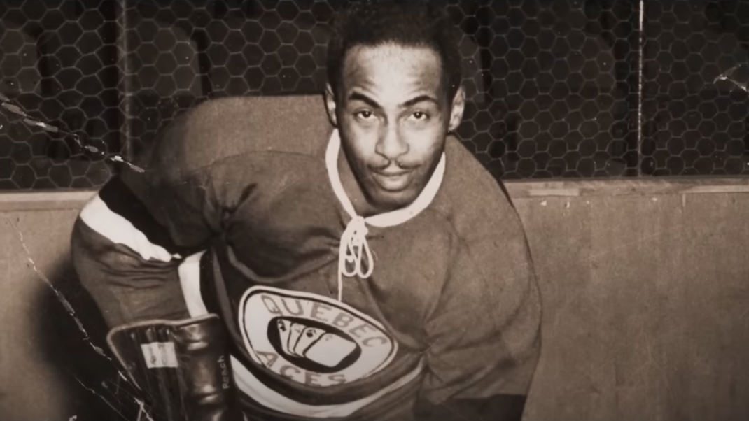 An archival monotone photo of Black hockey player Herb Carnegie in his Quebec Aces uniform, from BLACK ICE
