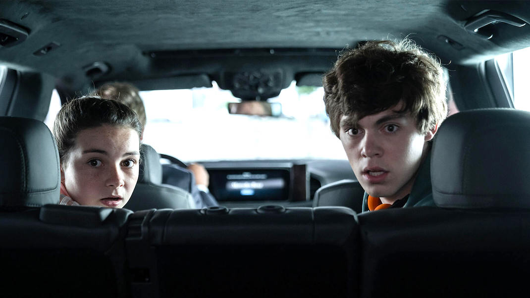 Two children (Lilly Aspell and Jack Champion) stare fearfully out the back window of a car in RETRIBUTION (2023)
