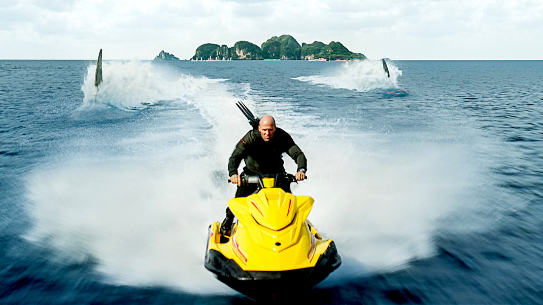 Jason Statham races on a Jet Ski ahead of two giant shark fins in MEG 2: THE TRENCH